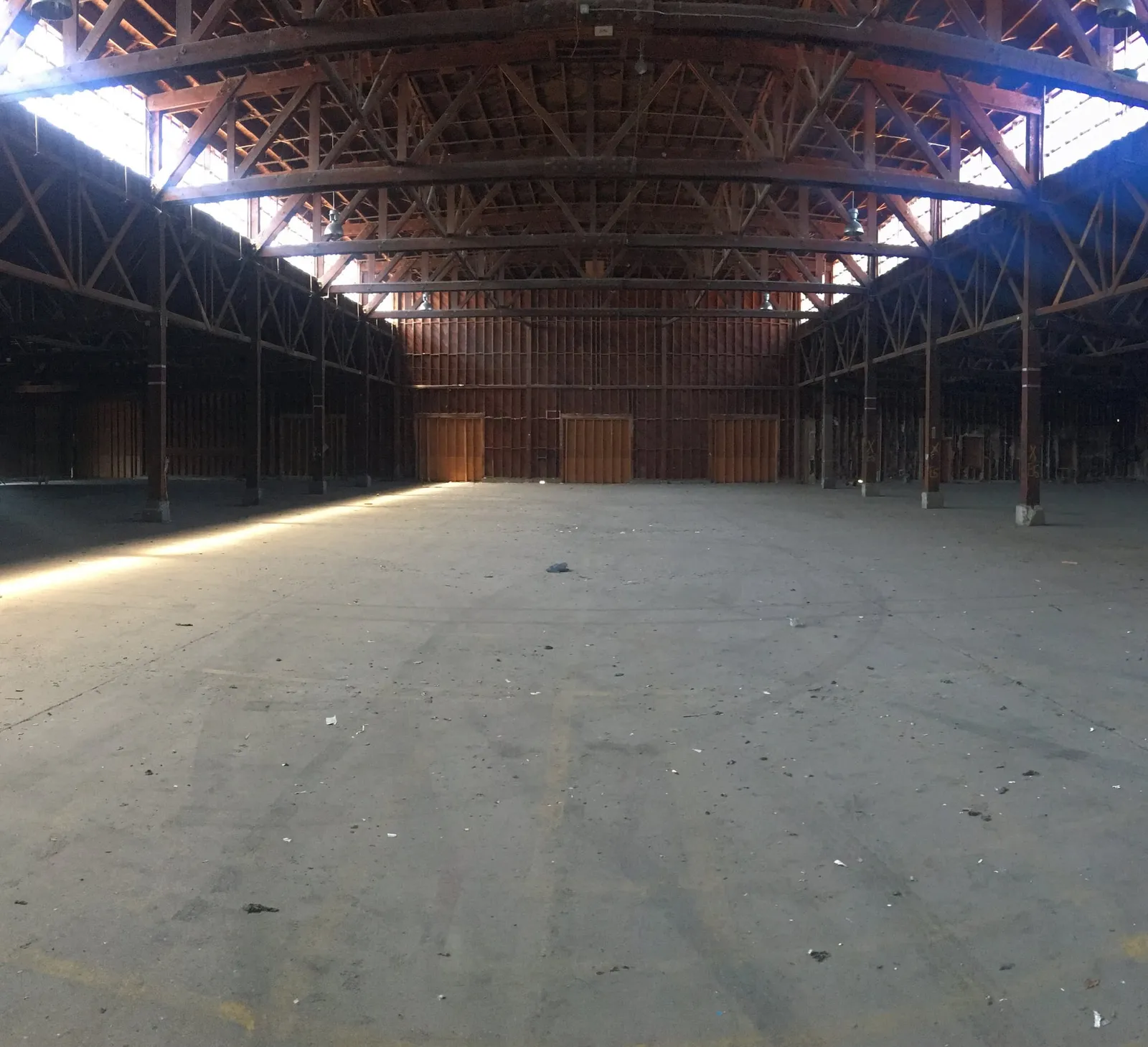 Inside, empty and waiting: a long concrete floor under rows of timber roof trusses.