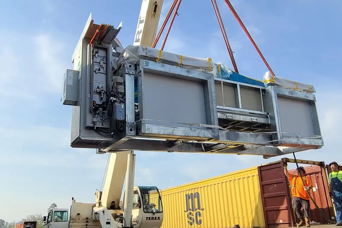 A new saw arrives: a crane lifts the machine off a flatbed truck as the crew guides it.