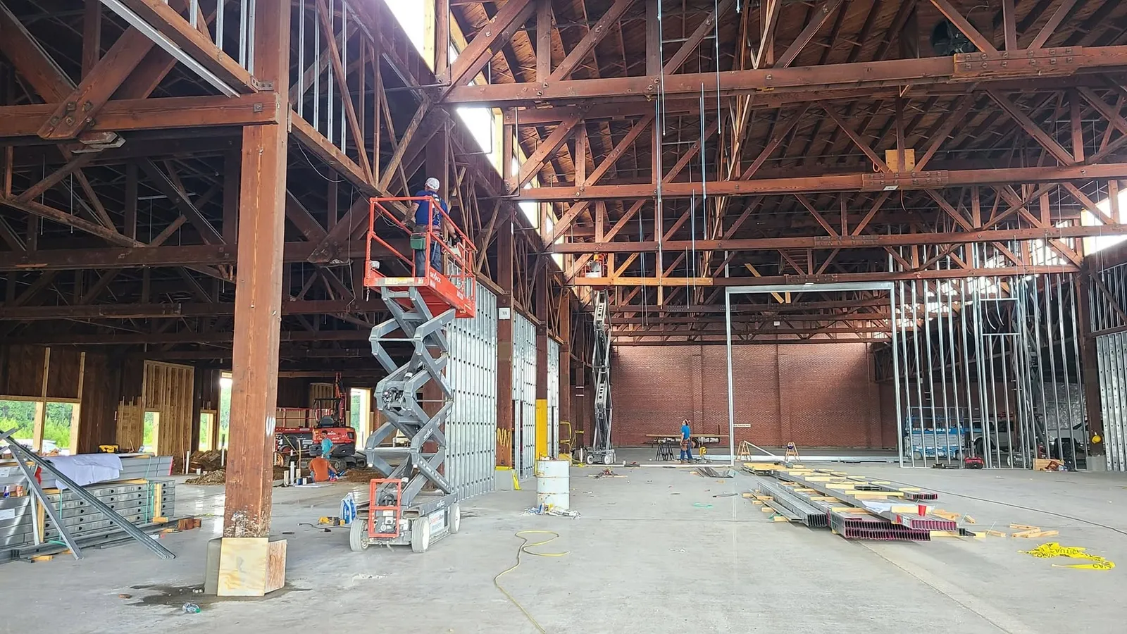 Work begins: a crew on a lift among the timber trusses as new walls are framed below.