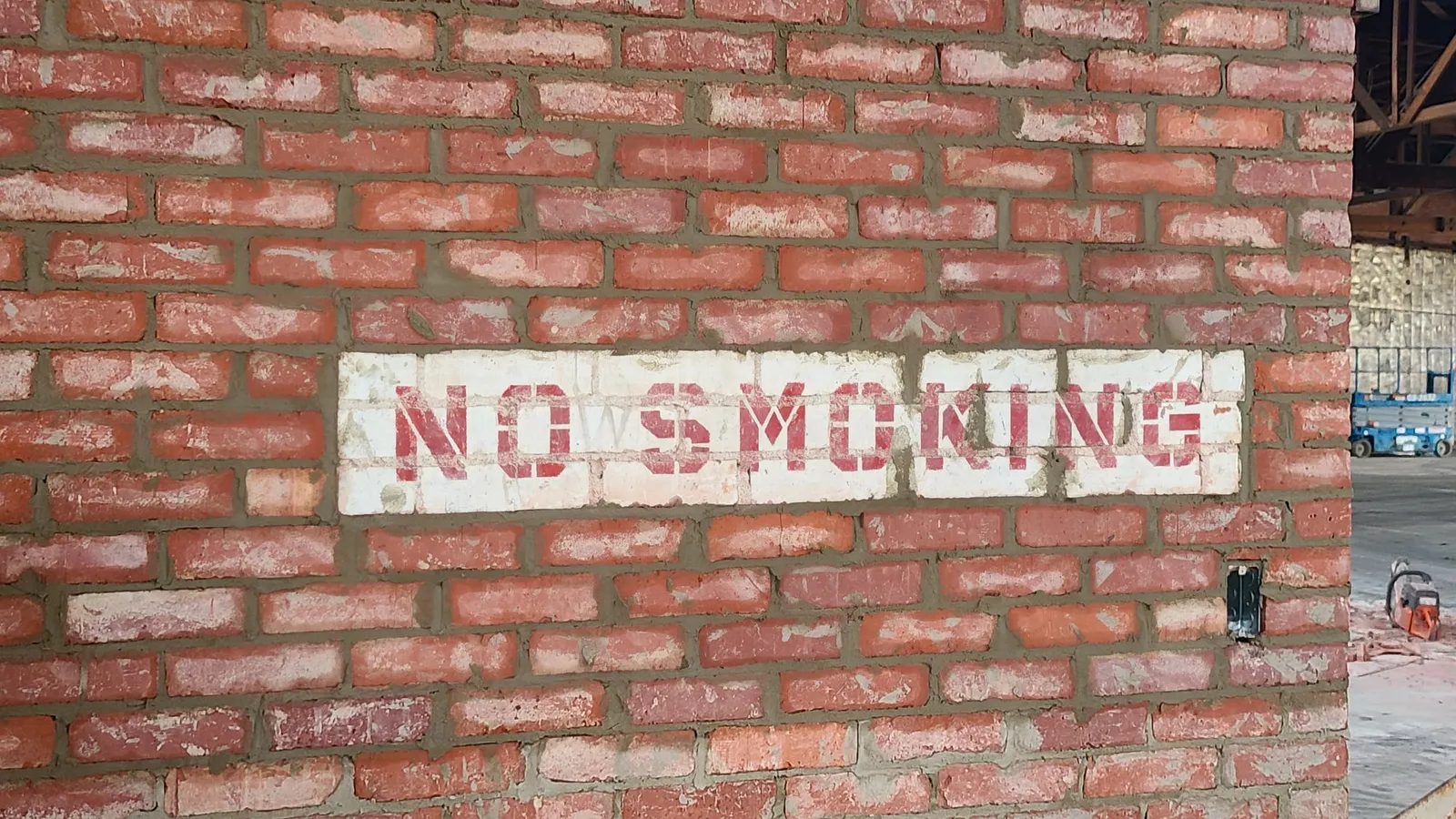 A piece of the past kept in place: an old painted “No Smoking” sign on the brick wall.