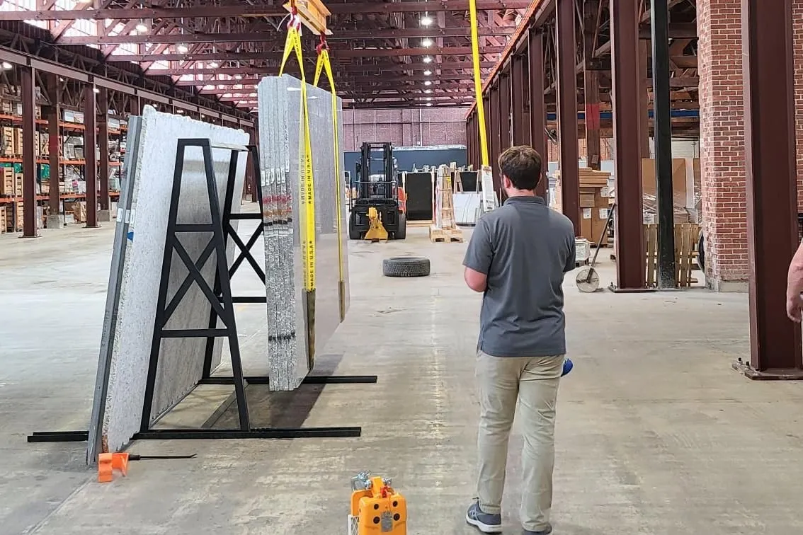 A slab is lifted by overhead crane and set on a rack in the slab gallery.