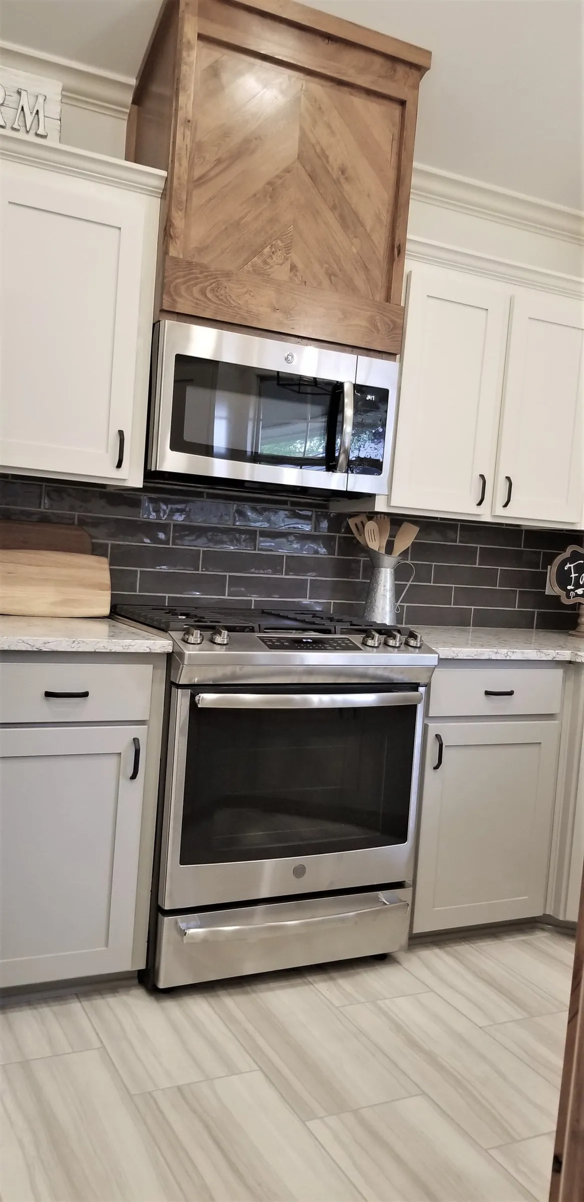 Stainless range below a wood range hood with a dark tile backsplash.