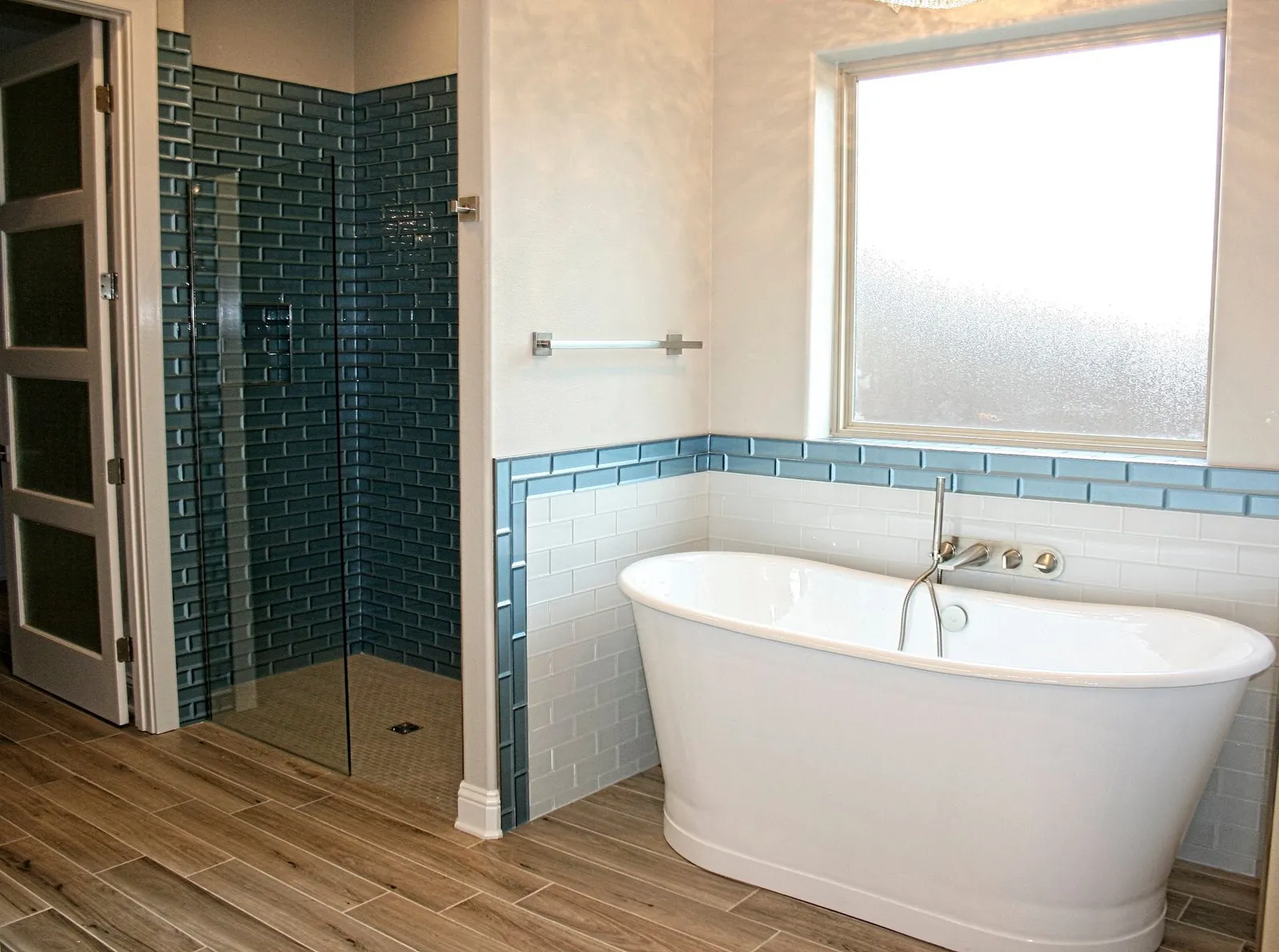 Primary bathroom with a freestanding tub, a blue tile accent band and a shower in deep blue tile.