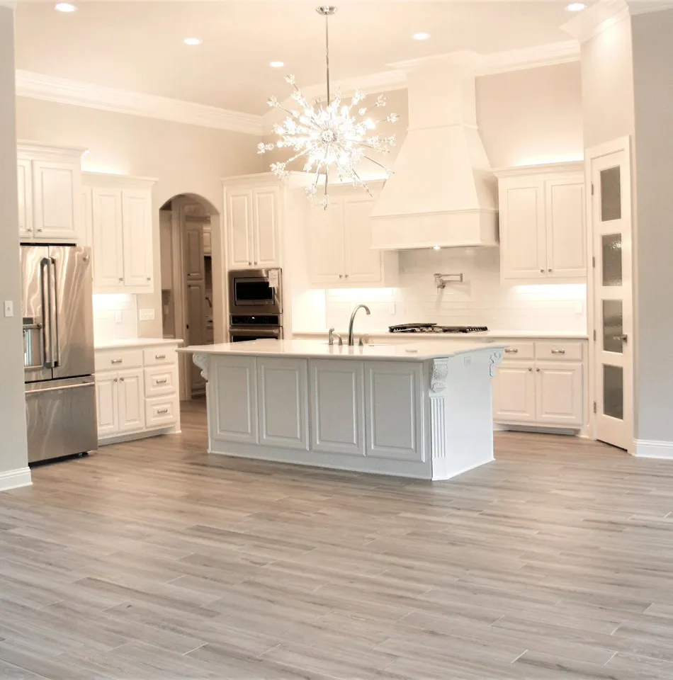 White kitchen with a large quartz island under a starburst chandelier and wood-look tile floors.