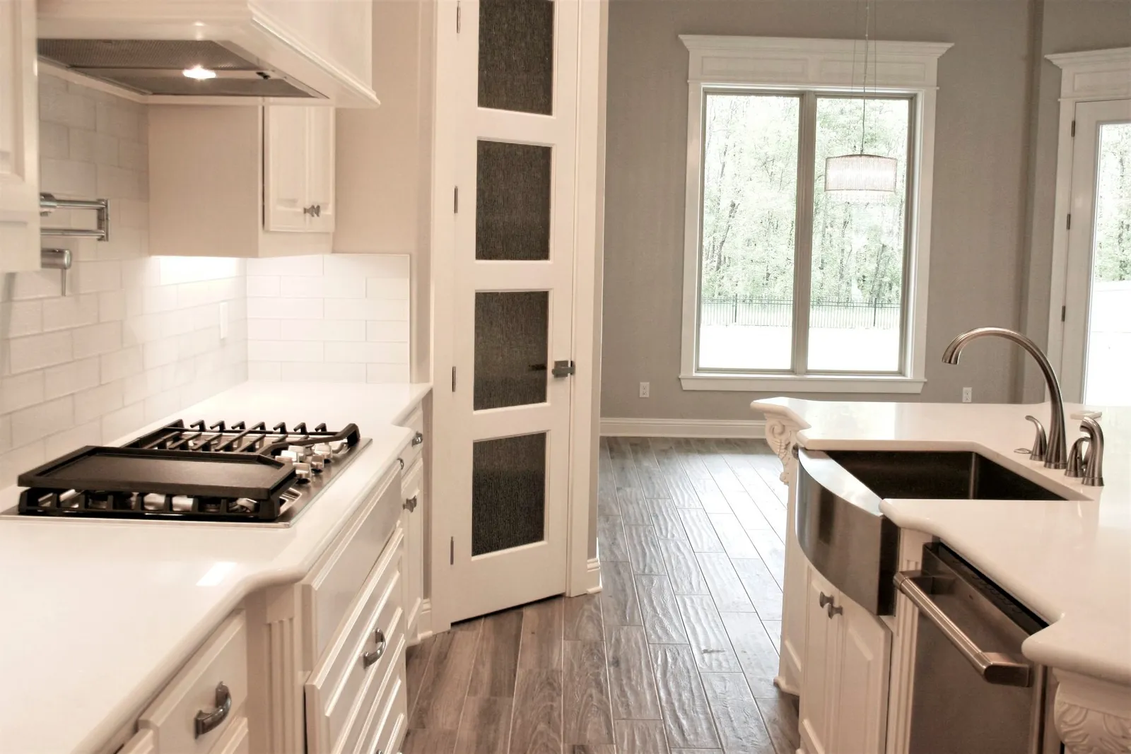 Kitchen with a gas cooktop, white cabinets and a sink under the window.