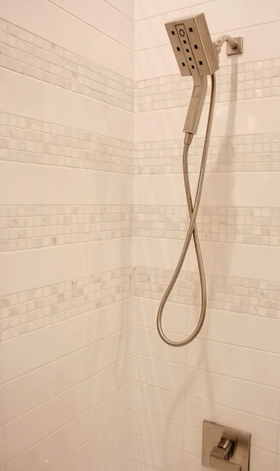 Shower with a handheld fixture and a decorative tile accent band.