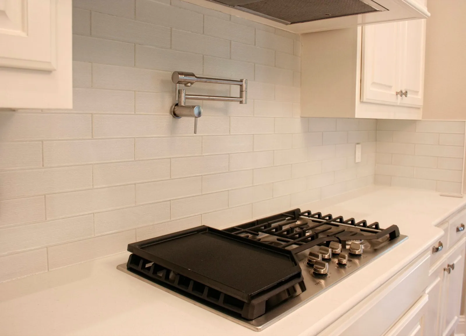 Gas cooktop and pot filler against a white subway tile backsplash.