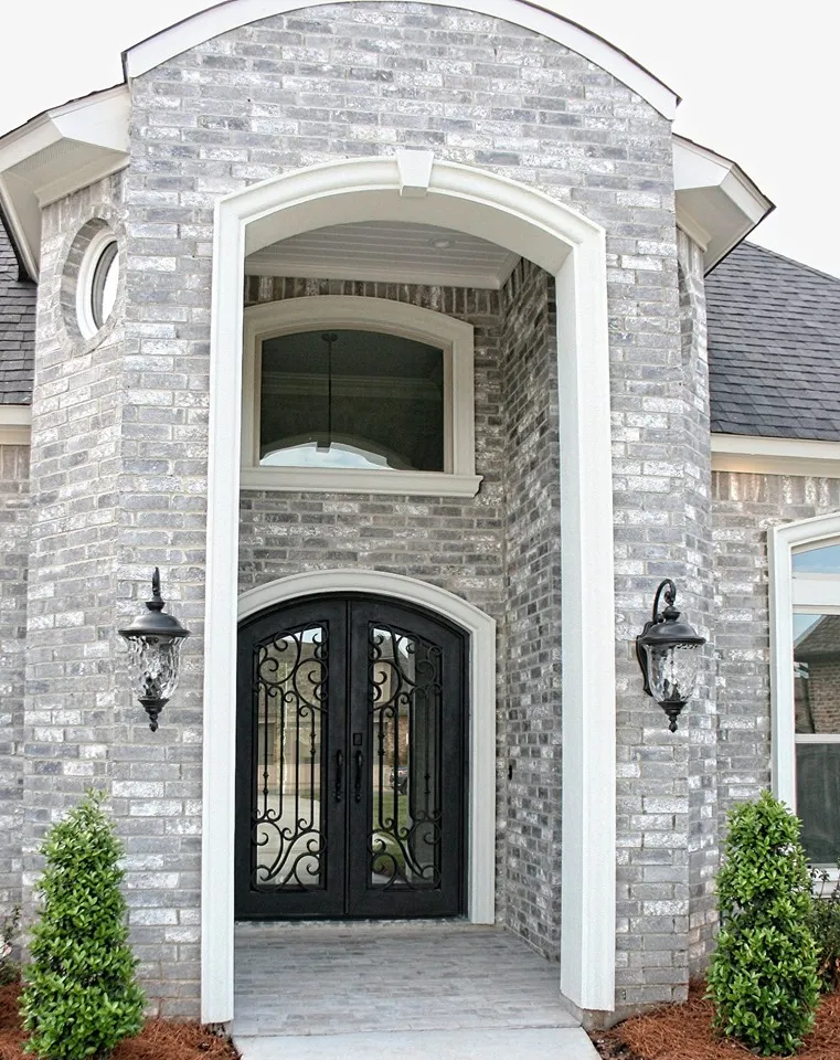 Stone and brick front entry with arched wrought iron doors.