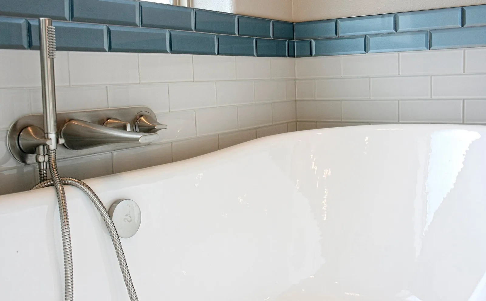 Close-up of a freestanding tub and handheld faucet below a blue tile band.