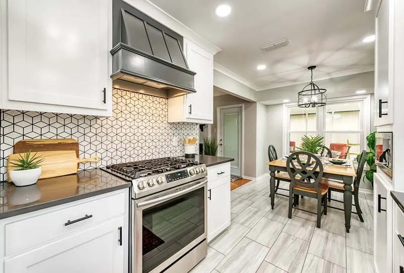 White kitchen with a geometric cube-pattern backsplash, gray countertops and a gray range hood.