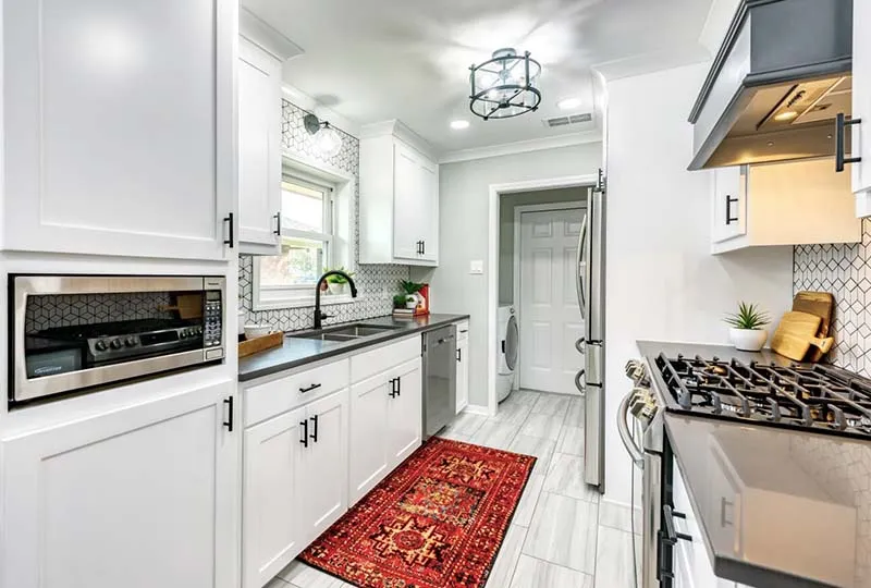 View through the white kitchen with gray countertops and wood-look tile floors.