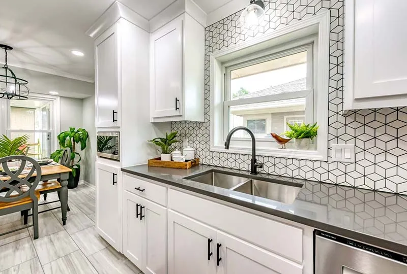 Sink under a window framed by white geometric backsplash tile.
