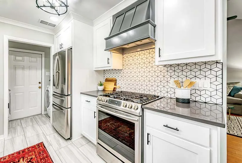 Stainless range under a gray hood with the geometric tile backsplash.