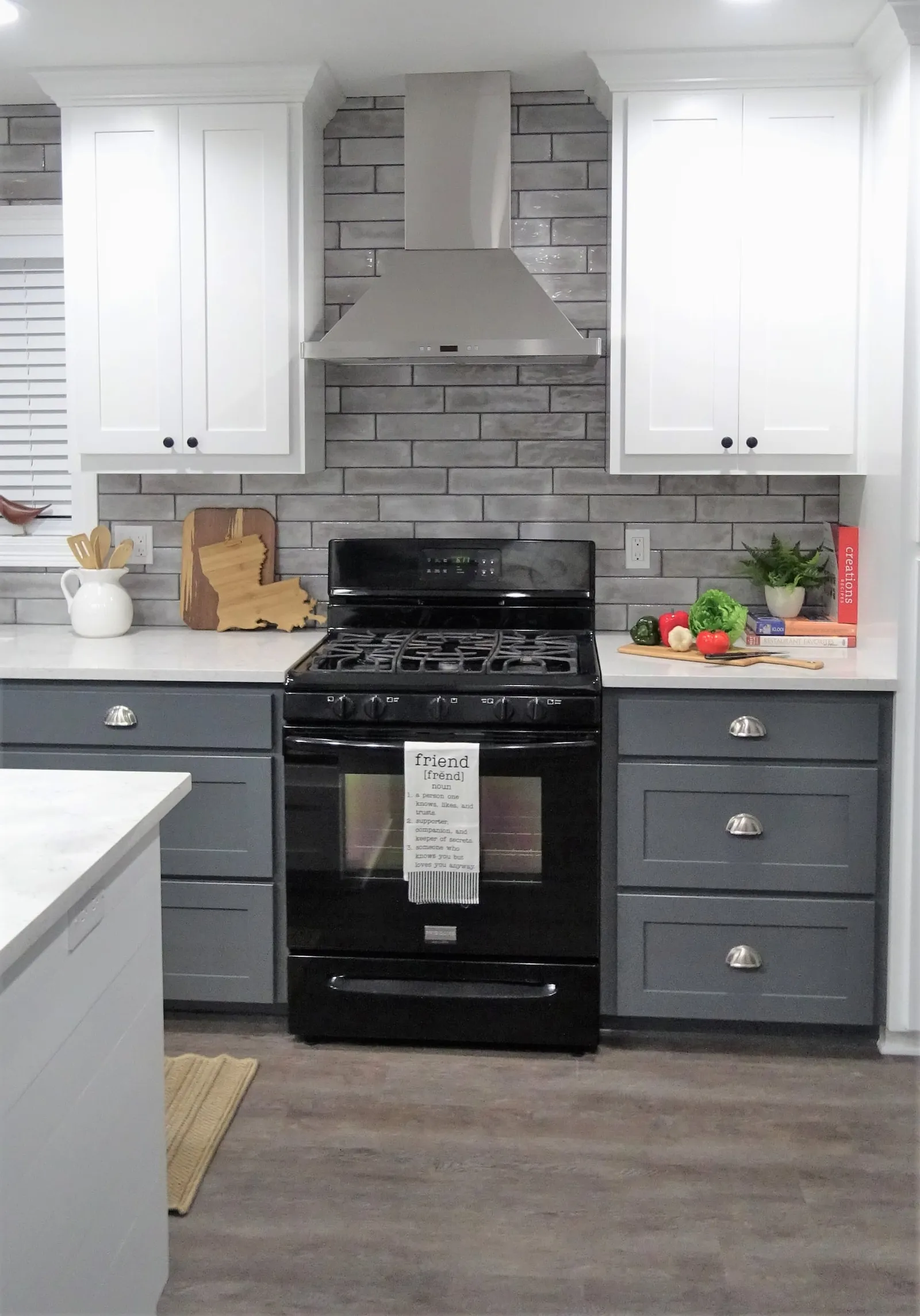 Black range under a stainless hood with a gray brick-look tile backsplash.