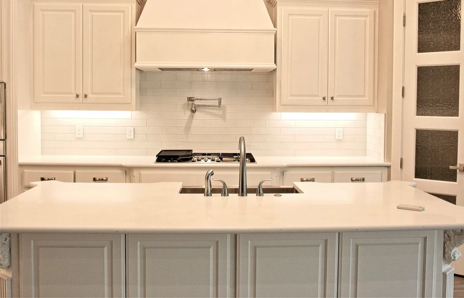 White quartz island and countertops with a white subway tile backsplash and pot filler.