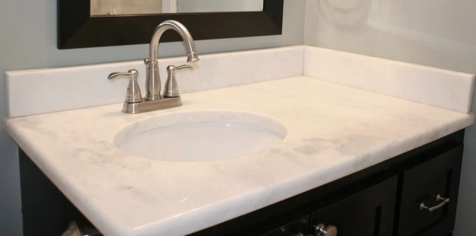 White marble vanity top with an undermount sink on a dark cabinet.