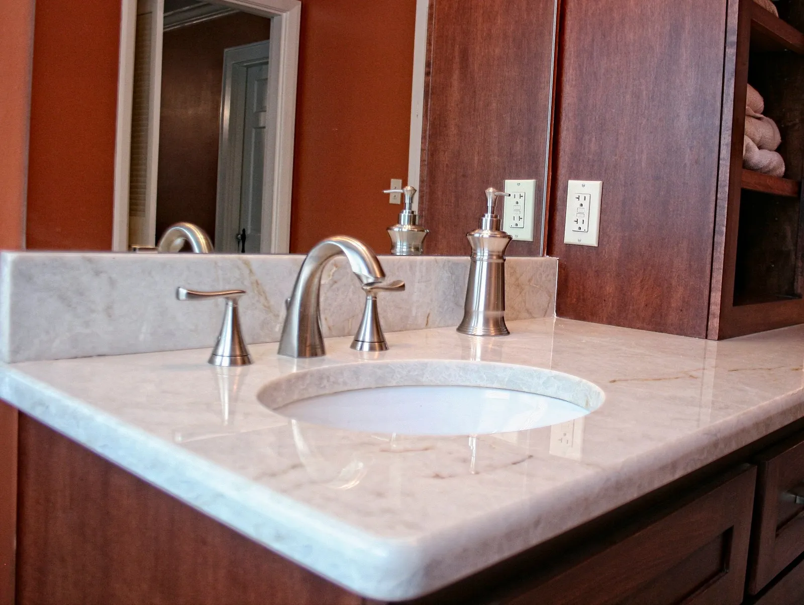 White marble vanity top with a brushed nickel faucet on a cherry vanity.