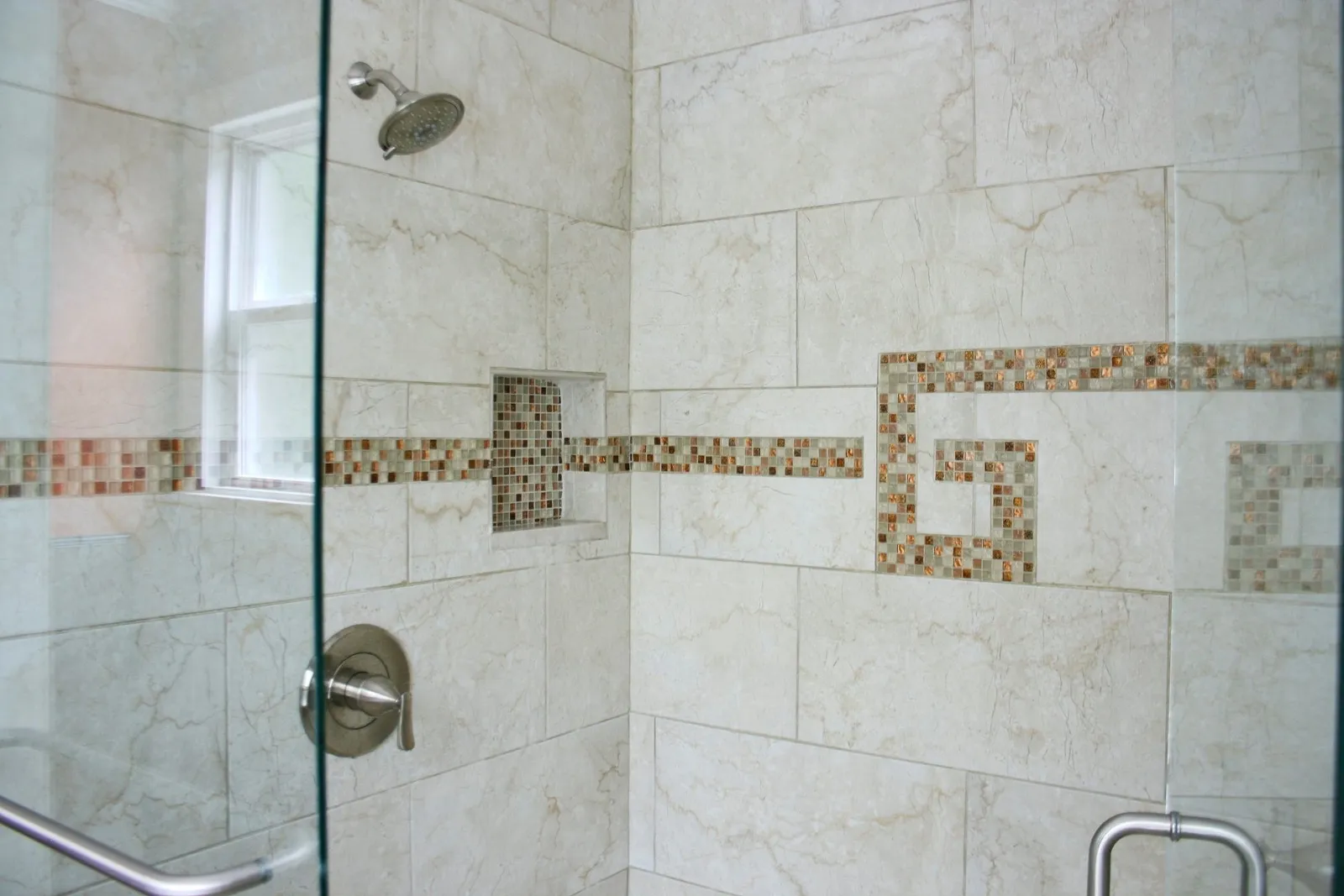 Glass shower with large marble-look wall tile and a mosaic Greek key accent band.