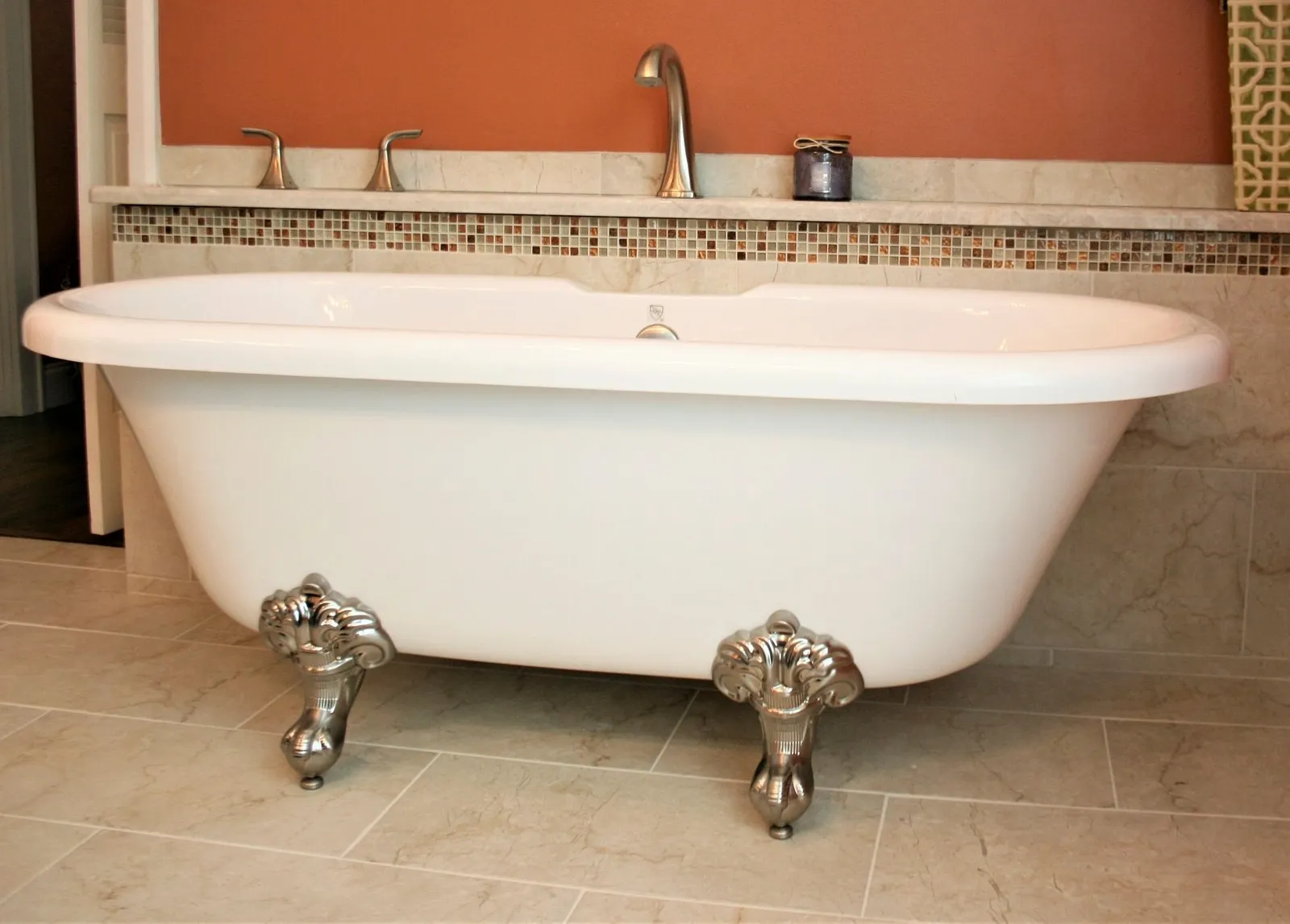 Clawfoot tub on a beige tile floor with a mosaic accent band on the wall.