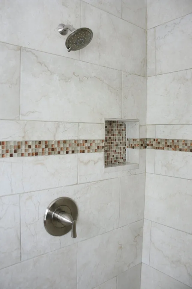 Shower wall in white marble-look tile with a mosaic band and a built-in niche.