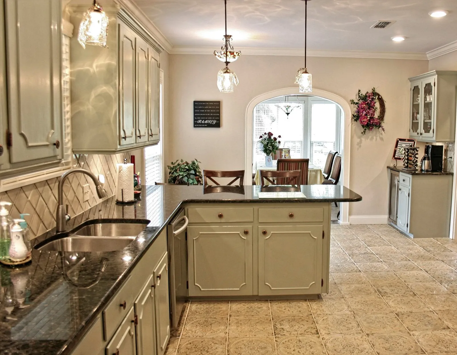 Kitchen with sage green cabinets, dark granite countertops and a patterned cream tile floor.
