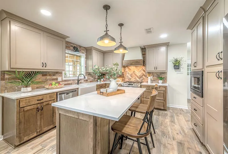 Kitchen island with a white countertop under industrial pendants, with a brick-look herringbone backsplash.
