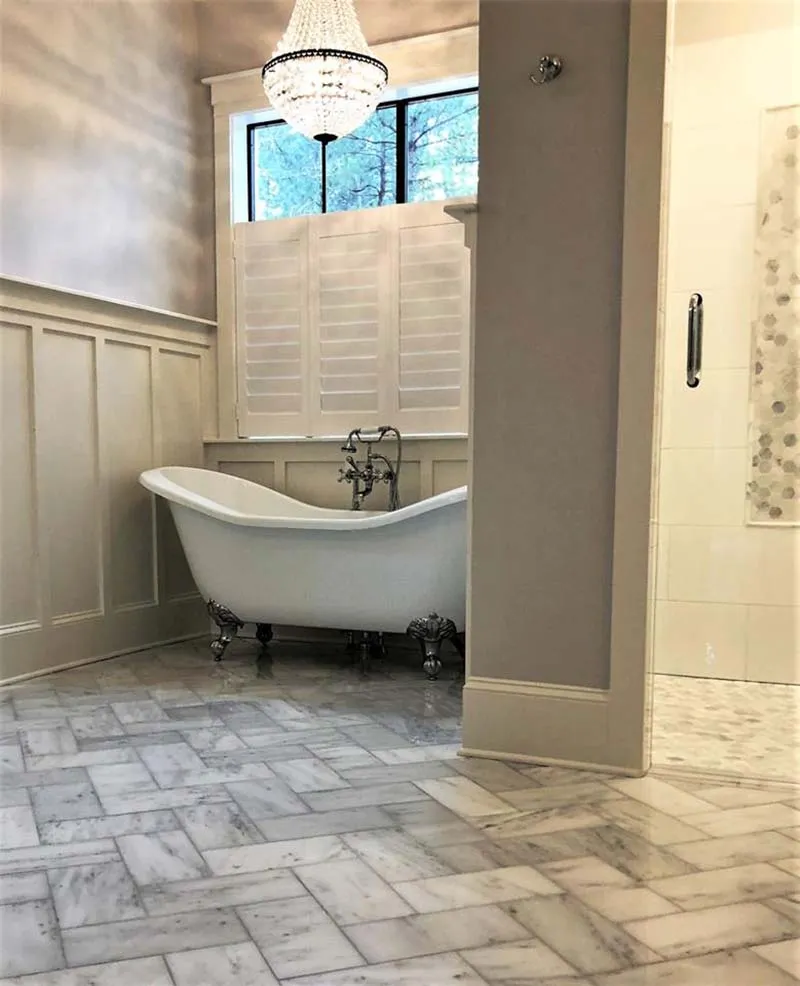 Freestanding clawfoot tub on a herringbone marble floor.