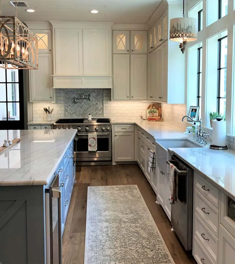White kitchen with marble countertops, a gray island and a patterned runner.