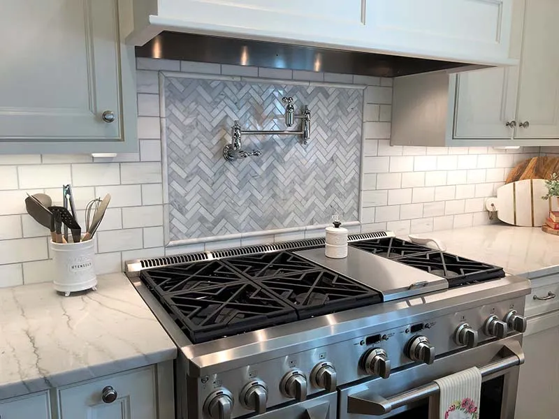Professional range in front of a marble herringbone backsplash panel framed by white subway tile.