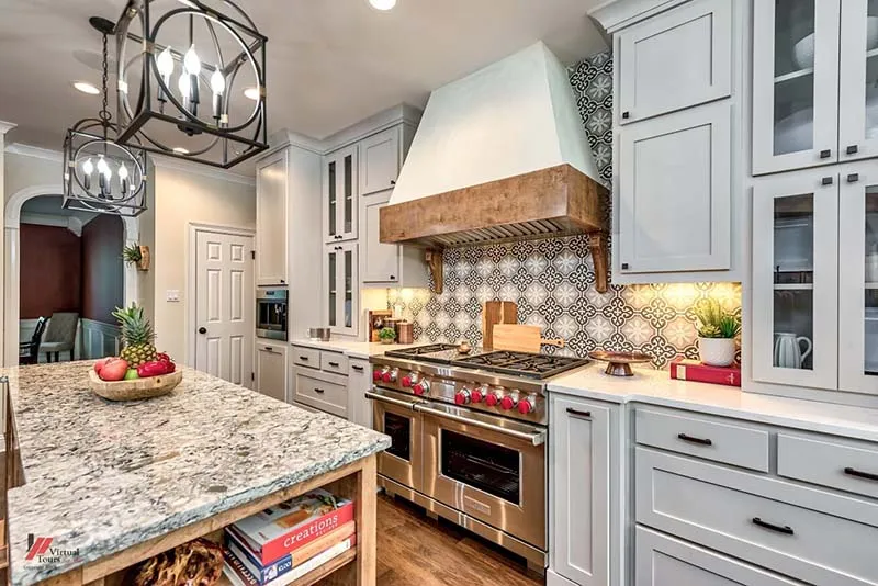 Kitchen with a granite island, gray cabinets and a patterned tile backsplash behind the range.