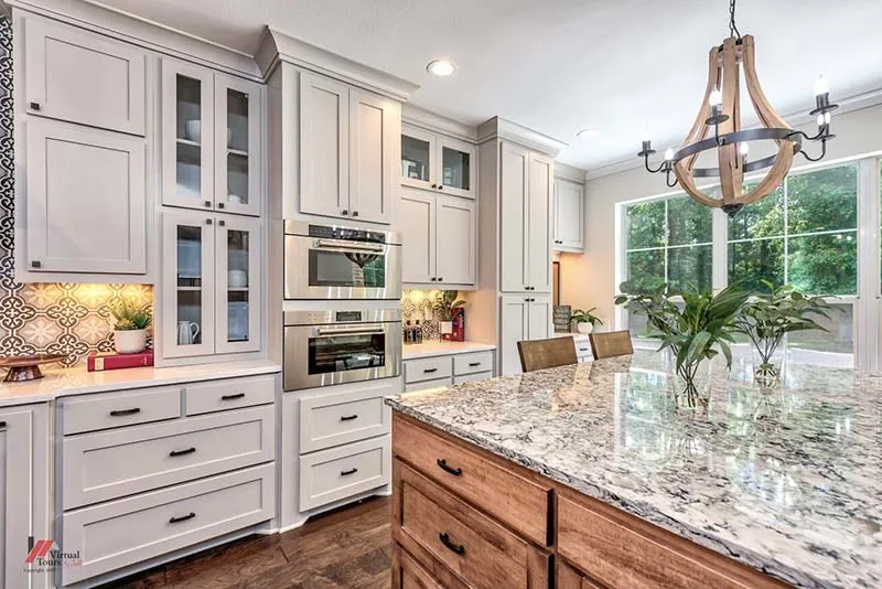 Gray cabinets and a patterned backsplash beside a granite island under a wood chandelier.