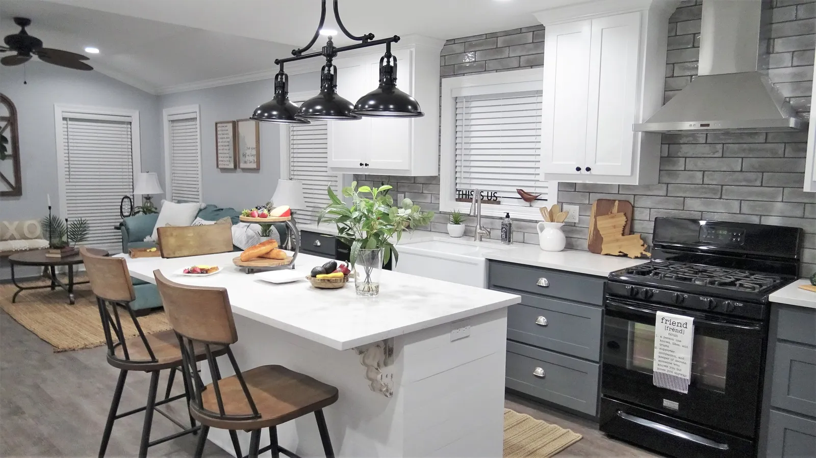 White quartz island with wood stools, dark gray lower cabinets and a gray brick-look backsplash.