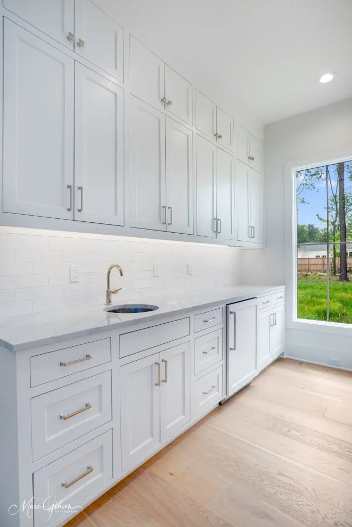 Wall of white cabinets with a bar sink and a quartzite countertop on light wood floors.