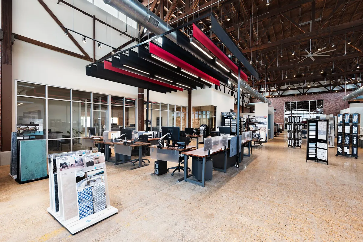 Our designers' desks on the showroom floor, under red and black ceiling panels and the building's timber trusses, with tile sample displays all around.