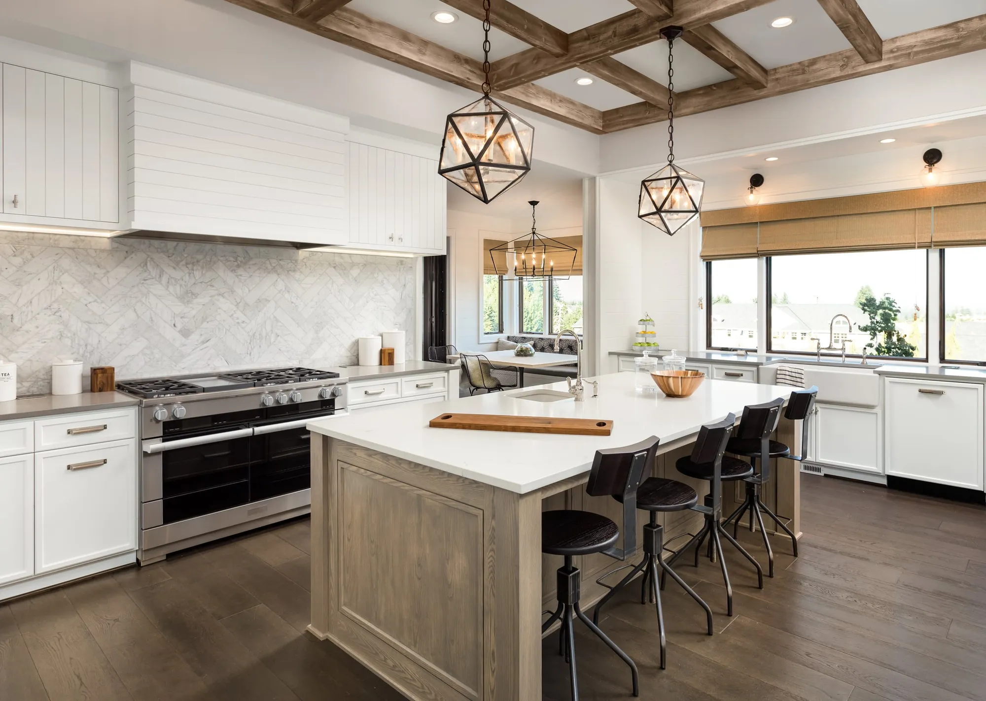 Bright white farmhouse kitchen with a marble herringbone backsplash, a wood island with black stools, and geometric pendant lights.