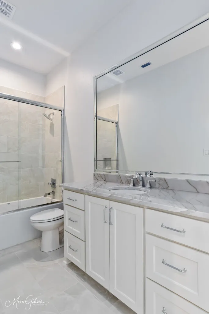 Guest bathroom with a quartzite vanity top and a tub with a sliding glass door.