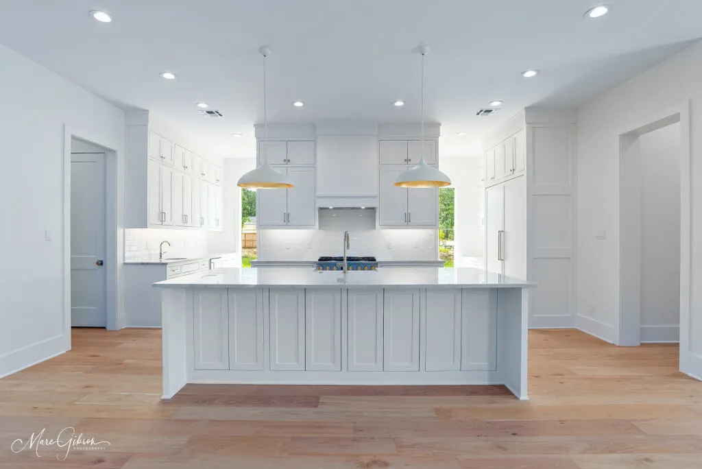 White kitchen with a large quartzite island, two brass pendant lights and light wood floors.