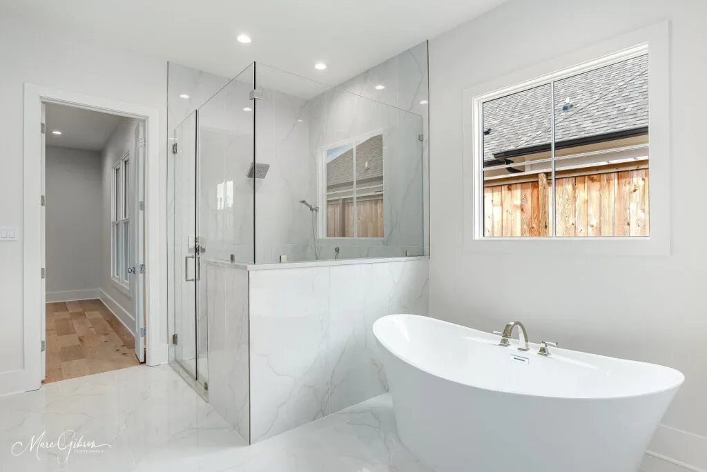 Primary bathroom with a freestanding tub, a frameless glass shower and large marble-look floor tile.