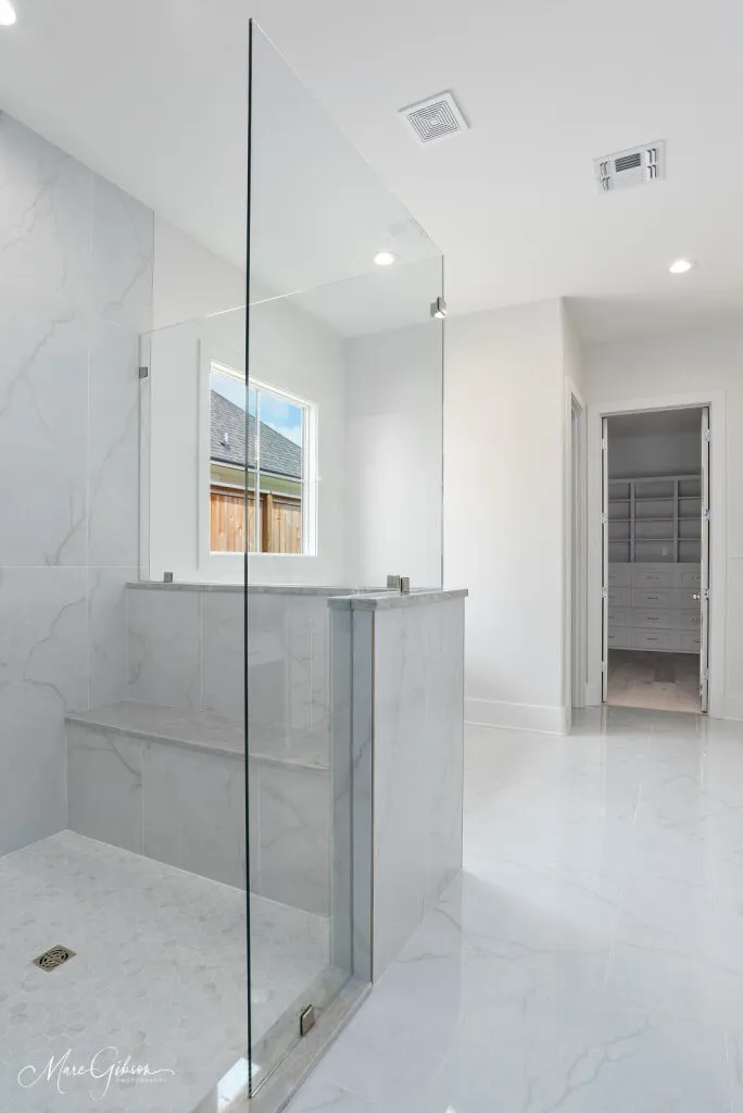 Frameless glass shower with marble-look wall tile, a bench and a matching tile floor.