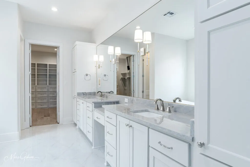 Long white double vanity with quartzite countertops, opening to a walk-in closet.