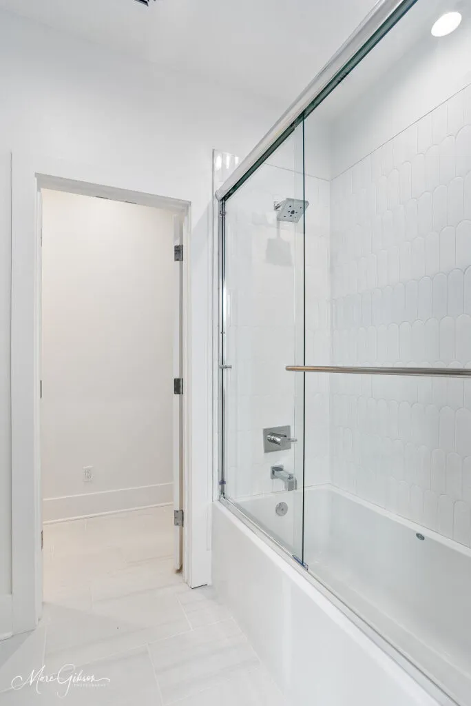 Tub with a sliding glass door and white tile walls.