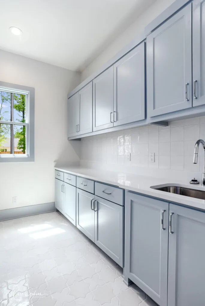 Utility room with blue-gray cabinets, a quartzite countertop and sink, and a white tile backsplash.
